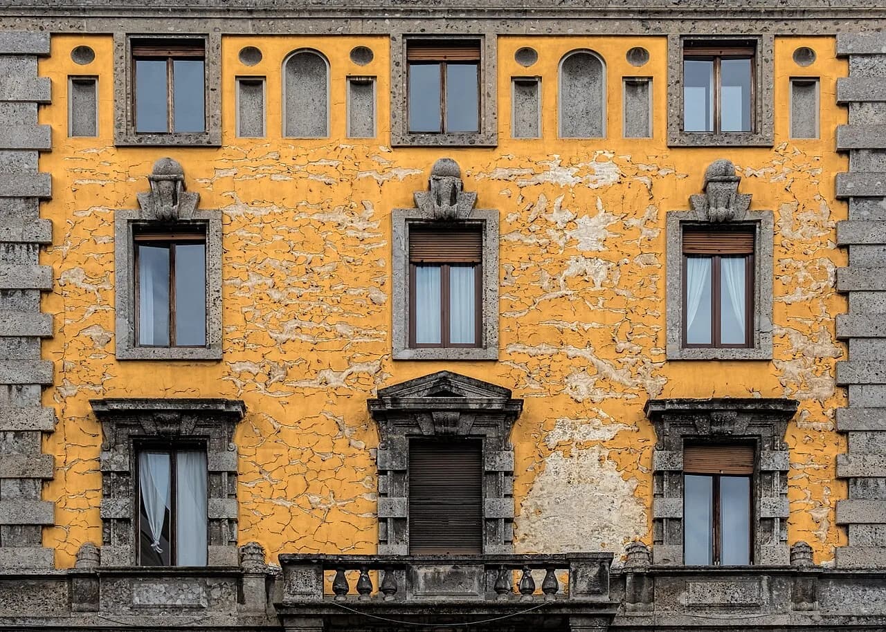 Finestre e intonaco giallo sulla facciata di un edificio residenziale a Milano.